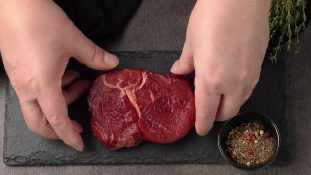 Cook add salt pepper and thyme to fresh raw beef steak meat for grilling, top view close up — Stock video