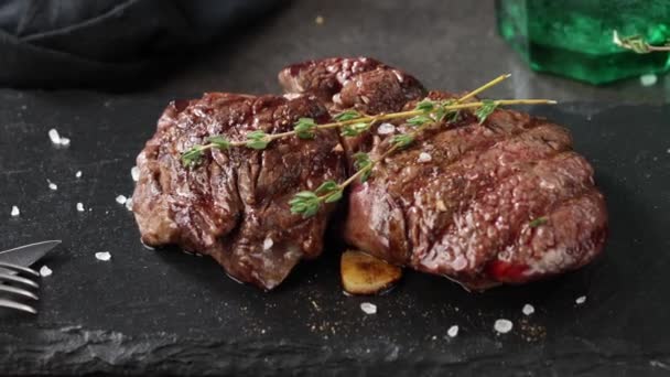 将新鲜烤牛肉牛排与调料一起放在黑色石板上 上视率放大 — 图库视频影像