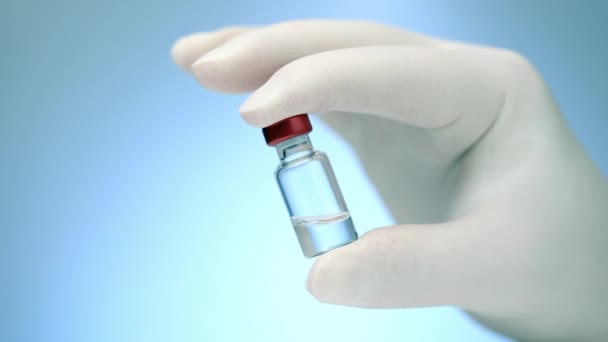 Закрытие бутылки медицинской вакцины в руках врачей на синем фоне — стоковое видео