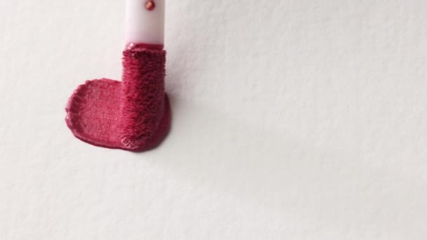 Ροζ καλλυντικό lip gloss επίχρισμα παράδειγμα εφαρμόζεται σε λευκό φόντο με ένα πινέλο απλικατέρ κοντά — Αρχείο Βίντεο