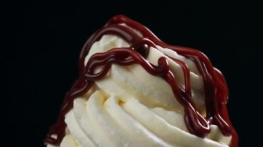 Erimiş çikolata sosu siyah arka planda çırpılmış kremanın üzerinde akıyor.