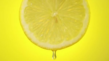 Taze sıkılmış limon suyu olgun meyve dilimlerinden akar. Sarı arka planda yakın plan.