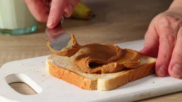 Les mains des femmes appliquent la crème de beurre d'arachide sur une tranche de pain grillé fermer - vers le haut. cuisine maison petit déjeuner — Video