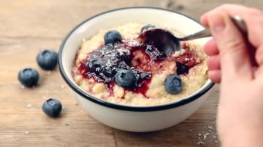 Bir kaşıkla el, sağlıklı taze pişmiş yulaf lapası, reçel ve taze yaban mersinli kahvaltılık kaseden taze yaban mersini alır. ev yemeği 