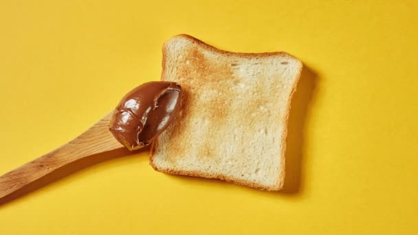 Primer plano de pan tostado con crema de chocolate sobre fondo amarillo, vista superior, stop motion — Vídeos de Stock