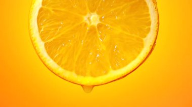 Olgun meyve diliminden taze sıkılmış portakal suyu damlaları portakal rengi arka planda yavaş çekimde yakın plan çekilir.