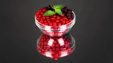 Amelanchier ve kırmızı frenk üzümü siyah aynada cam bir tabakta. Döngü hareketi. Yan görüş. Rotasyon 360. 4K UHD video görüntüsü 3840X2160