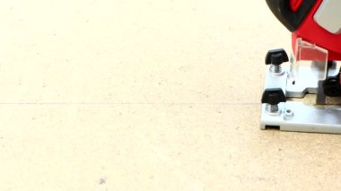 Bir marangoz elektrikli testereyle kontrplak kumaşı testereyle keser. Testereyle yakın plan çekimde çalışıyorum. Elektrikli yapboz ve kontrplakla çalışan marangoz ustası. 4K UHD video görüntüsü 3840X2160