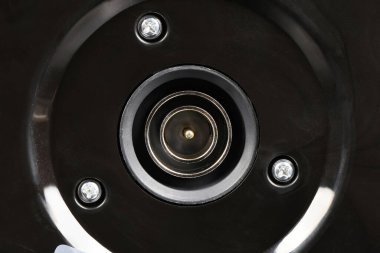 Direk tepemizde, modern siyah bir elektrikli su ısıtıcısının tabanındaki elektrik prizinin detaylı makro çekimi eşmerkezli metal lenikleri ve üç sağlam vidayı gösteriyor..