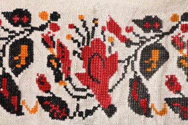 Beyaz keten üzerine el yapımı halk nakışları yakın plan. Kırmızı çiçekler ve turuncu aksanlı siyah yapraklı geleneksel çiçek süsü..