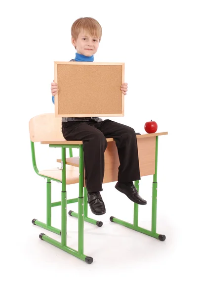 Menino sentado na mesa da escola e segurando bordo — Fotografia de Stock