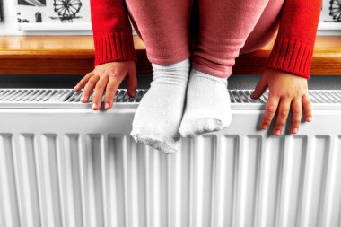 Küçük bir kız kaloriferde ellerini ve ayaklarını ısıtıyor.