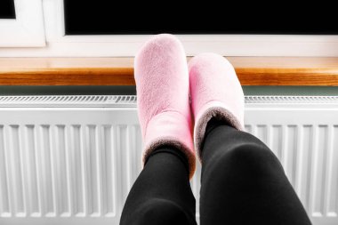 Kadın ellerini ve ayaklarını radyatörde ısıtıyor.