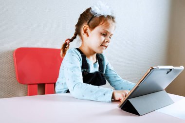 Çocuk okulda uzaktan çalışıyor, okula geri dönüyor. Küçük kız masada oturuyor.