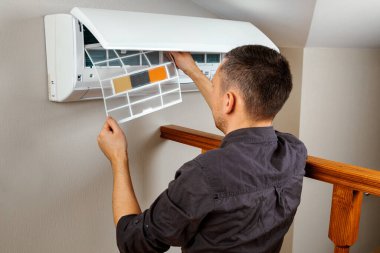 Erkek teknisyen içeride klimayı temizliyor.