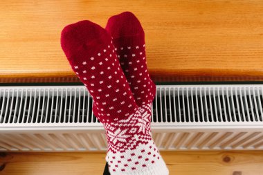 Kız ellerini ve ayaklarını radyatörde ısıtıyor.