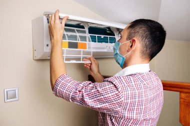 Erkek teknisyen içeride klimayı temizliyor.