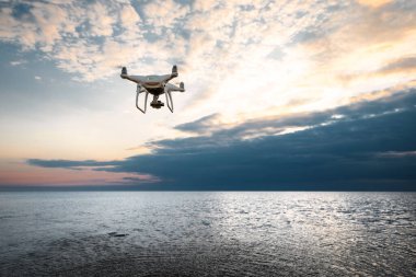 Deniz günbatımının arka planında uçan dron