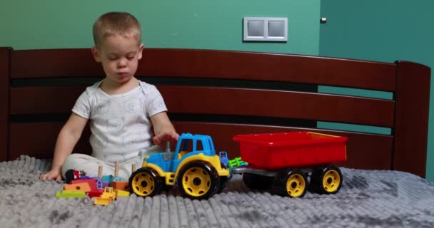 Szczęśliwy dziecko z zabawka ciągnik bawi się w łóżku w domu — Wideo stockowe