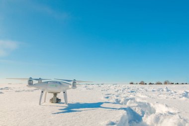 Güneşli kış gününde karla kaplı bir dron tarlanın üzerinde uçuyor.