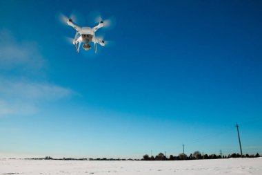 Güneşli kış gününde karla kaplı bir dron tarlanın üzerinde uçuyor.