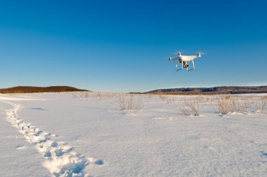 Güneşli kış gününde karla kaplı bir dron tarlanın üzerinde uçuyor.