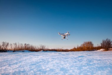 Güneşli kış gününde karla kaplı bir dron tarlanın üzerinde uçuyor.