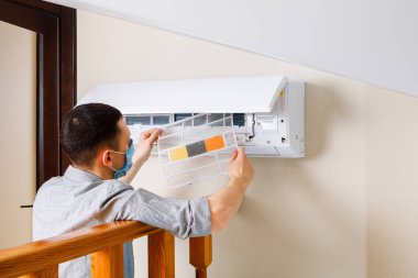Erkek teknisyen içeride klimayı temizliyor.