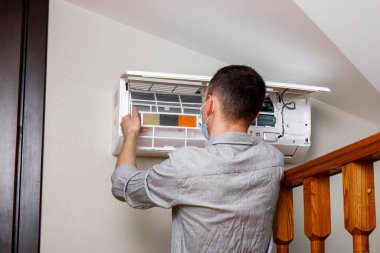 Erkek teknisyen içeride klimayı temizliyor.
