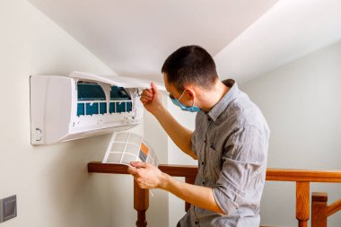 Erkek teknisyen içeride klimayı temizliyor.