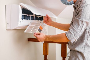 Erkek teknisyen içeride klimayı temizliyor.