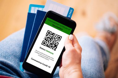 Cep telefonunu elinde tutan kadın bir elinde dijital aşı sertifikası, diğer elinde pasaport, maske ve bilet vardı.