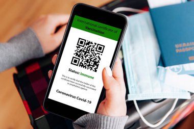 Cep telefonunu elinde tutan kadın bir elinde dijital aşı sertifikası, diğer elinde pasaport, maske ve bilet vardı.