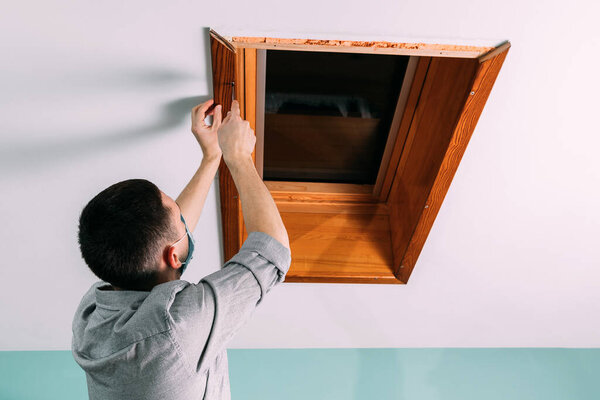 Рабочий устанавливает и проверяет окно на крыше в доме