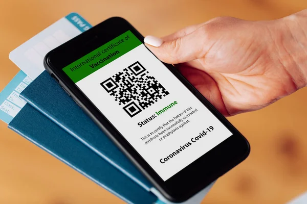 Cep telefonunu elinde tutan kadın bir elinde dijital aşı sertifikası, diğer elinde pasaport, maske ve bilet vardı.