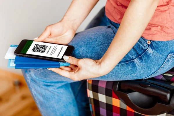 Cep telefonunu elinde tutan kadın bir elinde dijital aşı sertifikası, diğer elinde pasaport, maske ve bilet vardı.