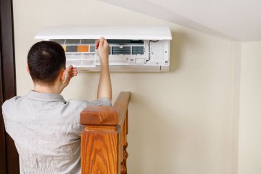 Erkek teknisyen içeride klimayı temizliyor.