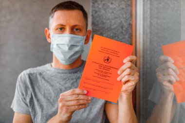 Erkek elinin üzerinde Almanca ve İngilizce metin bulunan uluslararası aşı sertifikası. Aşı kavramı