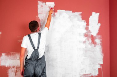 Adam duvarları ve tavanı beyaza boyuyor. Odayı boyuyor ve onarıyor..