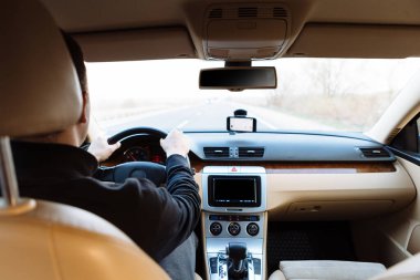 Genç adam asfalt yolda modern arabayı kullanıyor.