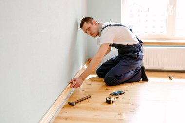 Onarım yapmak için. Yeni bir etek panosu kuruyorum. Bir adam odada tamirat yapar.