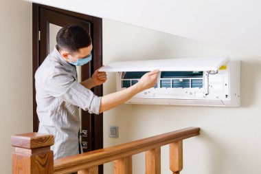 Erkek teknisyen içeride klimayı temizliyor.