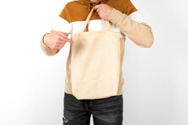 Genç adam beyaz arka planda beyaz tekstil eko çantası tutuyor. Tasarım için model