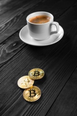 Tahta bir arka planda izole edilmiş kahve fincanının üzerinde duran kripto altın bitcoin.