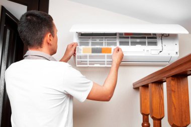Erkek teknisyen içeride klimayı temizliyor.