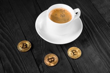 Tahta bir arka planda izole edilmiş kahve fincanının üzerinde duran kripto altın bitcoin.