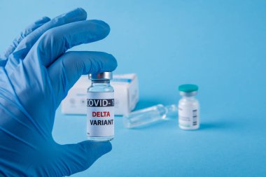 Kadın doktor elinde şırınga ve COVID 19 delta varyant aşısını mavi arka planda tutuyor. Sağlık ve Tıp Konsepti.