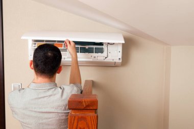 Erkek teknisyen içeride klimayı temizliyor.
