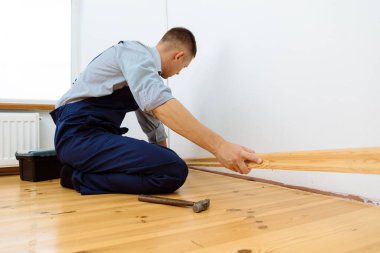 Onarım yapmak için. Yeni bir etek panosu kuruyorum. Bir adam odada tamirat yapar.