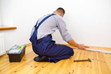 Onarım yapmak için. Yeni bir etek panosu kuruyorum. Bir adam odada tamirat yapar.